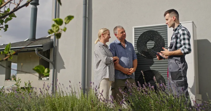 Fachberater erklärt einem Paar die Wärmepumpe vor dem Haus